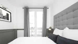 Een hotelkamer met een groot bed, grijze gordijnen, een ingelijst schilderij aan de muur en uitzicht op een balkon.