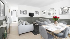 Ett modernt vardagsrum med en grå soffa, ett matbord för fyra personer och en platt-TV som är monterad på väggen.