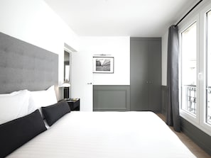 Een moderne hotelkamer met een groot bed, een nachtkastje met een lamp, een lijst met een afbeelding aan de muur, en uitzicht op het balkon.