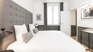 Ein modernes Hotelzimmer mit einem großen Bett, einem Nachttisch, einer Lampe, einem gerahmten Bild an der Wand und einem Fenster mit Vorhängen.