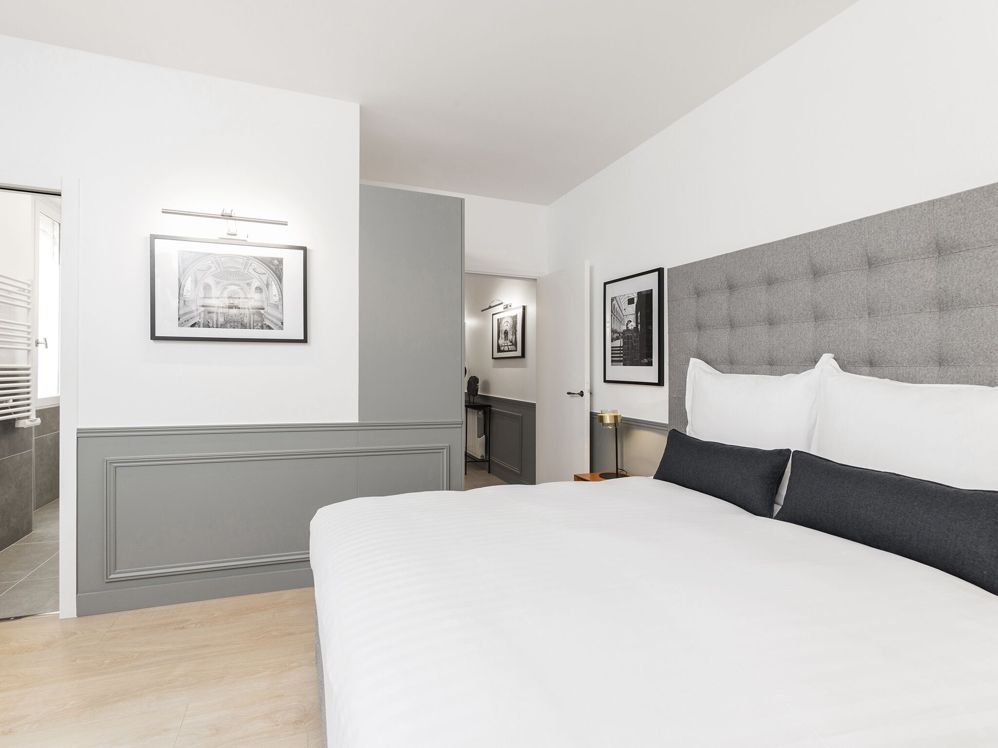 Une chambre d’hôtel moderne avec un grand lit, une tête de lit grise et des tableaux encadrés accrochés aux murs.