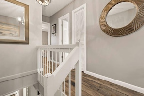 A staircase with white railings, a round mirror with a geometric frame, and a framed picture on the wall.