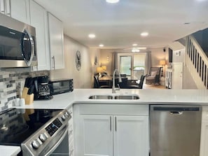 A modern kitchen with a built-in oven, microwave, and dishwasher, a dining area with a chandelier, and a staircase leading to another level.