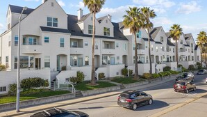 A row of modern, multi-story residential buildings with white exteriors and dark roofs, lined with palm trees and a street with parked cars. - Classic Santa Cruz Getaway! (Santa Cruz)
