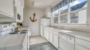 A kitchen with white cabinets, a stove, a refrigerator, and a window with curtains. - Classic Santa Cruz Getaway! (Santa Cruz)