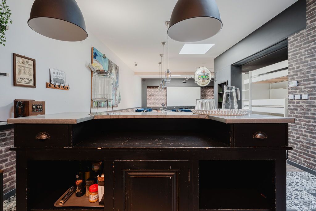 A kitchen with a black countertop, two pendant lights, a hanging light fixture, a brick wall, and a window.