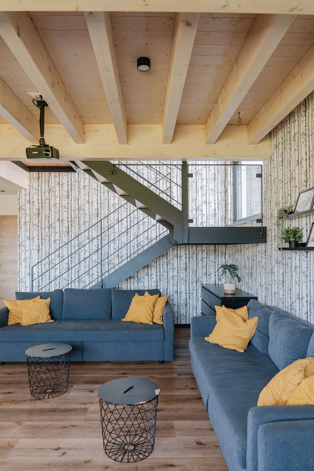 Un soggiorno moderno con un divano blu, una scala e un proiettore a soffitto.