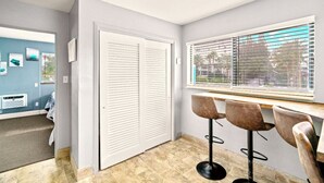 A room with a closed white door, a window with blinds, a wooden table, and three bar stools.
