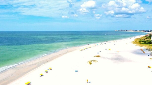 A beach with white sand, clear turquoise water, and a few umbrellas.