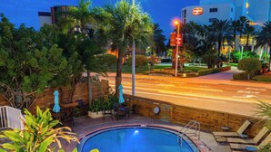 A swimming pool with a wooden deck, surrounded by palm trees and chairs.