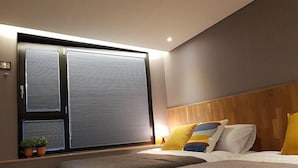 A modern bedroom with a large bed, a wooden headboard, and a window with blinds. - Hostel Cleo Seoul Hongdae (Seoul)