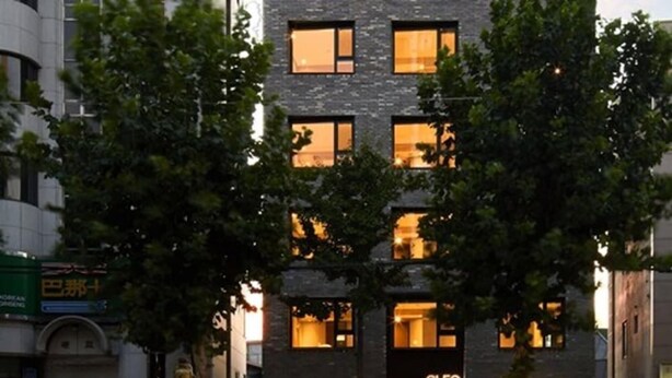 A modern building with multiple floors, featuring a prominent entrance with a glass door and illuminated signage. - Hostel Cleo Seoul Hongdae (Seoul)