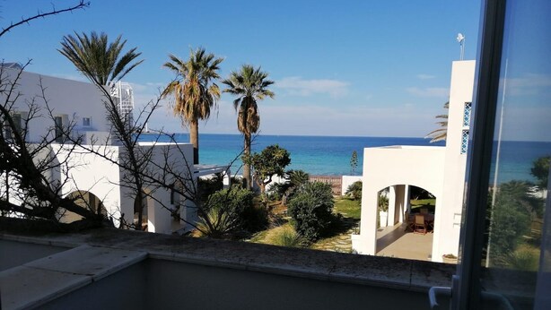Uitzicht vanaf een balkon op een kustgebied met palmbomen en een helderblauwe lucht.