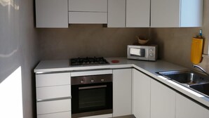 A compact kitchen with white cabinets, a gas stove, a microwave, and a sink. - Villa Azzurra facing the sea (SAN VITO LO CAPO)