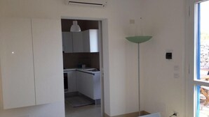 A modern kitchen with white cabinets, a dining area with a table, and a view through an open doorway. - Villa Azzurra facing the sea (SAN VITO LO CAPO)