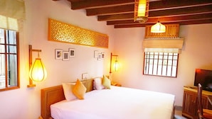 A bedroom with a large bed, wooden headboard, two wall-mounted lamps, a window with bars, and a television on a wooden cabinet. - Lemongrass Homestay (Hoi An)