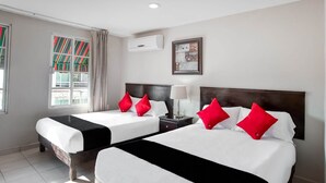Une chambre d’hôtel avec deux lits, chacun doté de draps blancs et d’oreillers rouges, une table de chevet avec une lampe, et une fenêtre avec des rideaux à rayures.