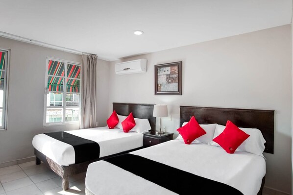 A hotel room with two beds, each with white bedding and red pillows, a bedside table with a lamp, and a window with striped curtains. - Boca Inn Hotel and Suites (Boca del Río)
