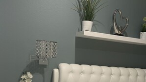 Ein Schlafzimmer mit einem gesteppten Kopfteil, einem weißen Nachttisch mit Pflanze und einer Wandleuchte.