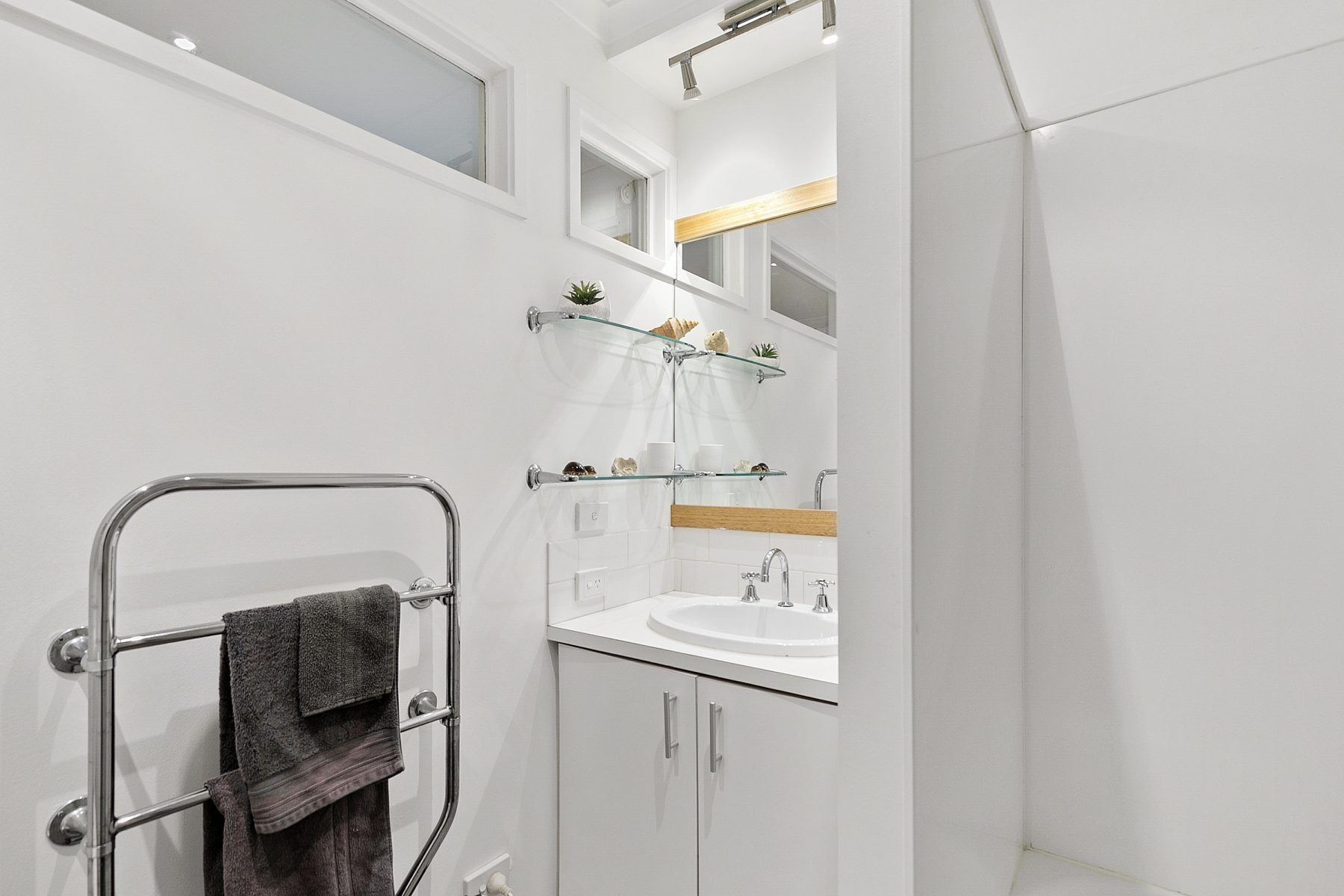 A modern bathroom with a glass shower enclosure, a towel rack, and a vanity with a mirror and shelves.