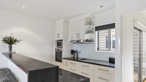 A modern kitchen with white cabinets, a black countertop, and a built-in oven. - Coastal Home away from Home (Torquay)