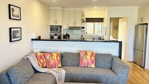 A modern living room with a grey sectional sofa, colorful throw pillows, and a kitchen in the background. - Coastal Home away from Home (Torquay)