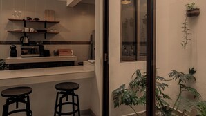 Et moderne køkken med en hvid bordplade, to sorte barstole, en trækasse og et vindue med udsigt.