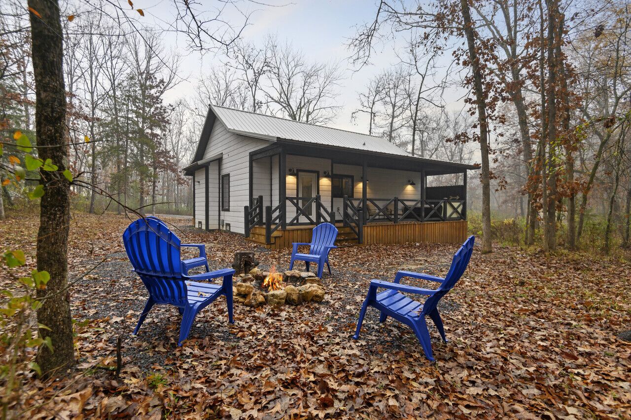 Une cabane avec une véranda, un foyer et quatre chaises Adirondack bleues.