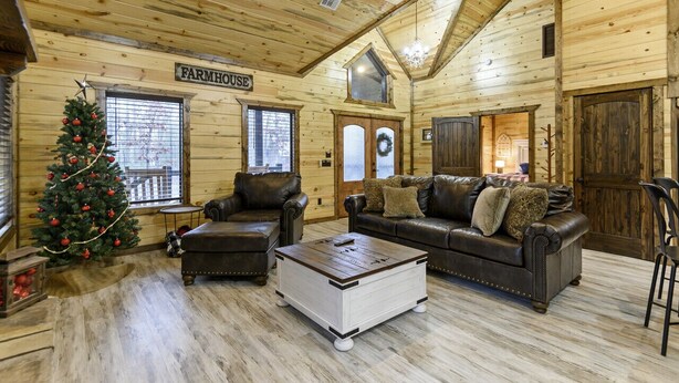 Ein Blockhaushaus-Interieur mit Kamin, Ledersofas, einem Weihnachtsbaum und einem Schild mit der Aufschrift 'FARMHOUSE'.
