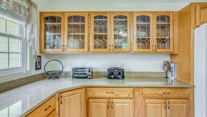 A kitchen with wooden cabinets, a granite countertop, and a window with curtains. - BEACH ISLAND BUM Cozy Cape Code, Pet Friendly Short, Walk to Beach! (Oak Island)