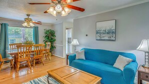A living room with a blue sofa, wooden coffee table, dining table with chairs, a ceiling fan, and a painting on the wall. - BEACH ISLAND BUM Cozy Cape Code, Pet Friendly Short, Walk to Beach! (Oak Island)