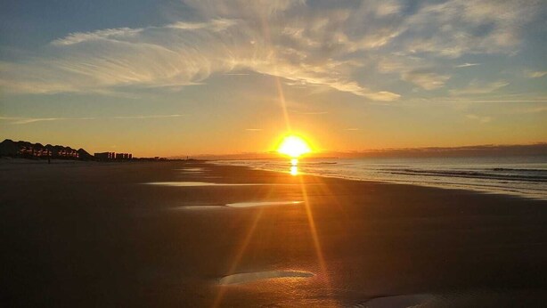 A sunset over a beach with a clear sky and distant buildings. - BEACH ISLAND BUM Cozy Cape Code, Pet Friendly Short, Walk to Beach! (Oak Island)