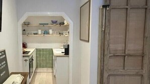 A narrow hallway leading to a kitchen with a green backsplash, a wooden door, and a desk with a chair.