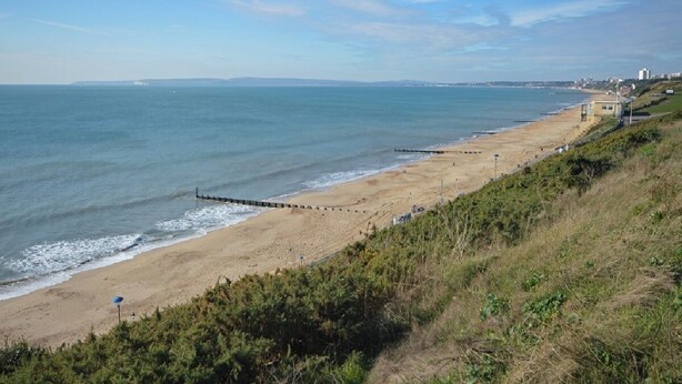 A coastal beach with a clear sky, a sandy shore, and a wooden jetty extending into the sea.