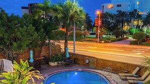 A swimming pool with a wooden deck, surrounded by palm trees and chairs.