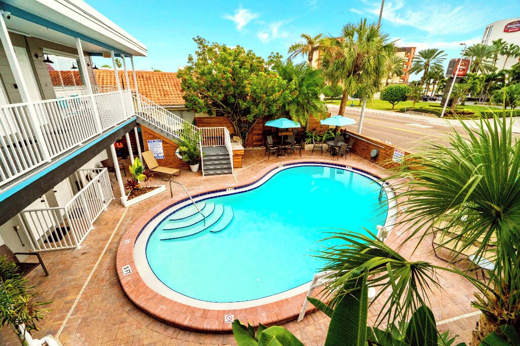 A swimming pool with a wooden deck, outdoor seating, and a staircase leading to an upper level.