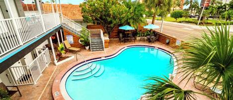 A swimming pool with a wooden deck, outdoor seating, and a staircase leading to an upper level.