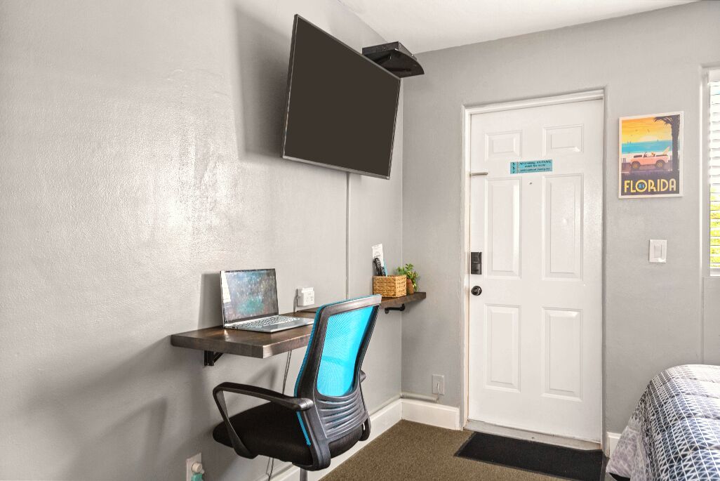 A room with a desk, chair, TV, door, and a Florida sign.
