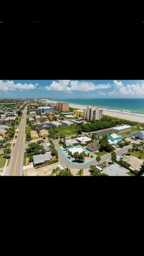 Vue aérienne d’une zone côtière avec une plage, des immeubles résidentiels et une grande piscine.