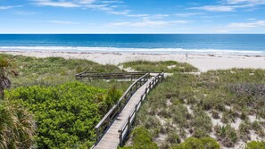 A wooden boardwalk leading to a beach with sand dunes and vegetation. -  ⛱️ BEACHFRONT PRIVATE BEACH HOUSE 🚀🌴👙🚢 (Cocoa Beach)