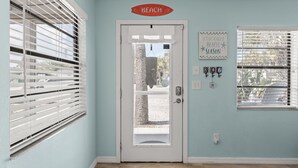 A room with a white door, a sign reading 'BEACH,' a calendar, and a window with blinds.