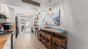 A modern kitchen with white cabinets, a wooden countertop, and a bar area with wicker stools.
