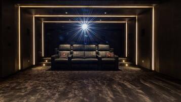 Una sala oscura con una pantalla grande, dos filas de sillones de cuero negro y un efecto de luz tipo explosión de estrellas sobre la pantalla.