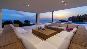 A modern outdoor seating area with a view of the ocean at sunset.