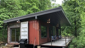 Una cabaña rústica con techo de metal, una terraza y una zona de barbacoa.