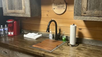 Eine rustikale Küche mit Holzschränken, einer Holzausziehtischplatte, einem Spülbecken, einer Kaffeemaschine und einem Schild mit der Aufschrift 'Adventure awaits'.