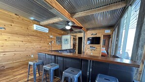 Un interior rústico con paredes de madera, una zona de bar con taburetes y un ventilador de techo.
