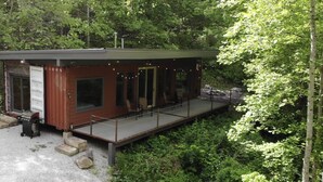 Una cabaña con terraza, rodeada de un bosque denso.