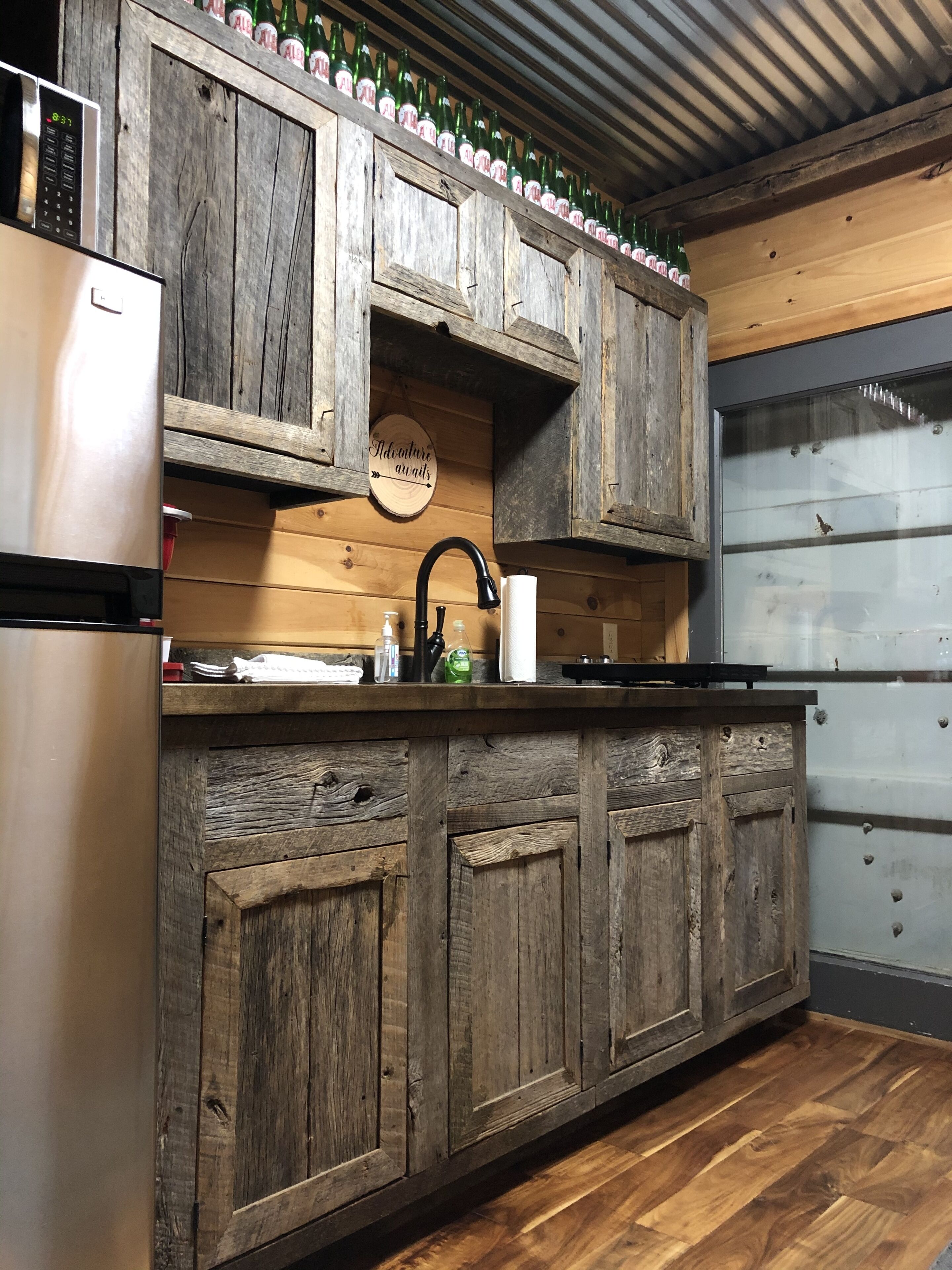 A rustic kitchen with wooden cabinets, a stainless steel refrigerator, and a wooden countertop.