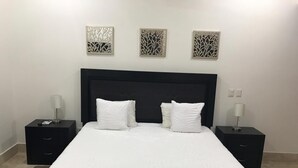 Un lit bien fait, avec une literie blanche et deux oreillers, flanqué de deux tables de chevet noires sur lesquelles sont posées des lampes.